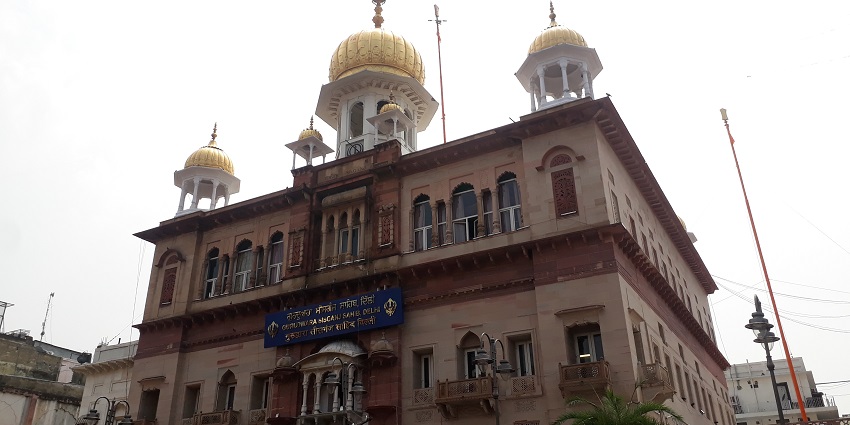 A picture of a Gurudwara in Delhi taken from outside with vehicles parked nearby