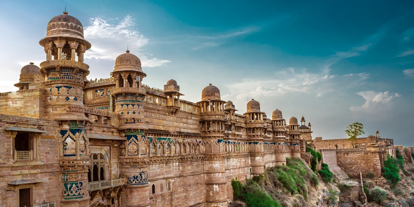 An ancient fort perched on a hill overlooking a city with thick walls and multiple towers.