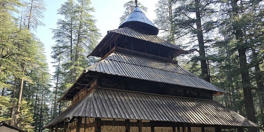 Hadimba Devi Temple surrounded by green trees on the mountains and devotees exploring