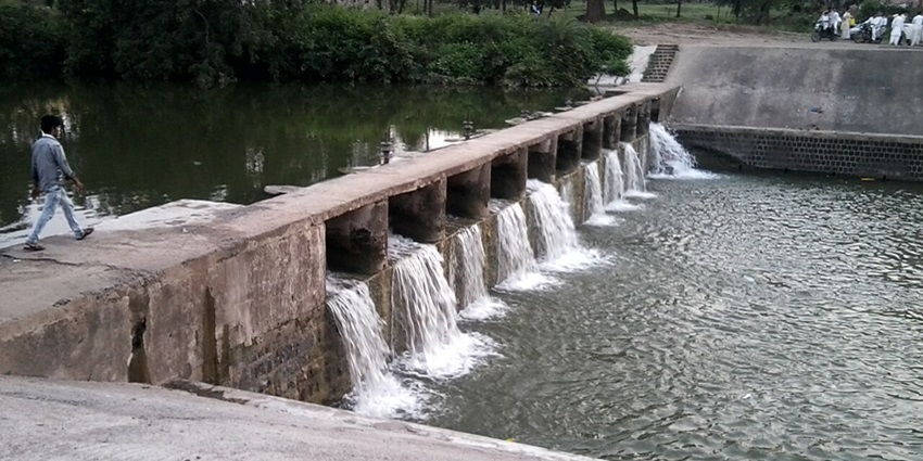 An image of a small dam structure, with the gates open and water flowing into the reservoir