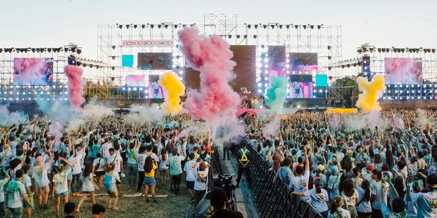 People gathering on a lush green field under daylight, enjoying music festival.