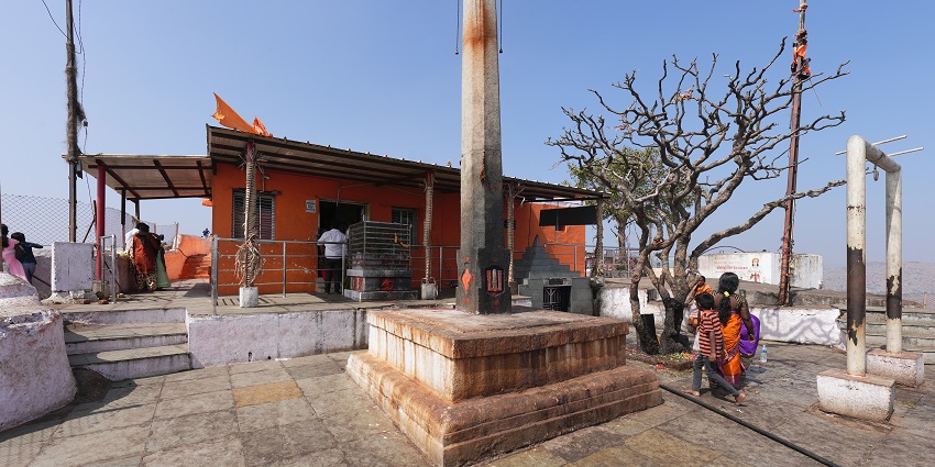 The image shows a large, vibrant statue of Lord Hanuman, a revered Hindu deity, standing in a temple setting.