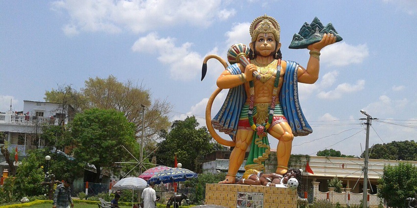 A giant statue of Lord Hanuman is standing tall in a garden surrounded by big trees.