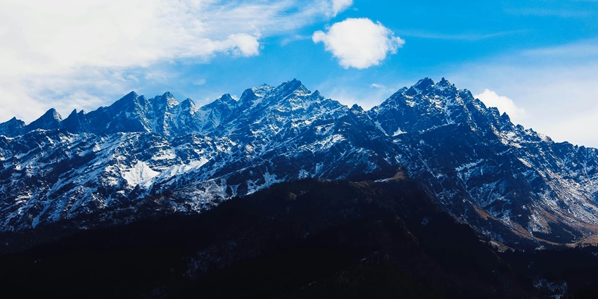 Mountain landscape under white clouds with clear blue sky during daytime.