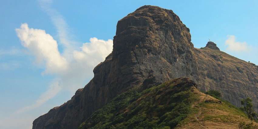 Majestic view of Harihar Fort with steep rock faces under a clear sky and wispy clouds.