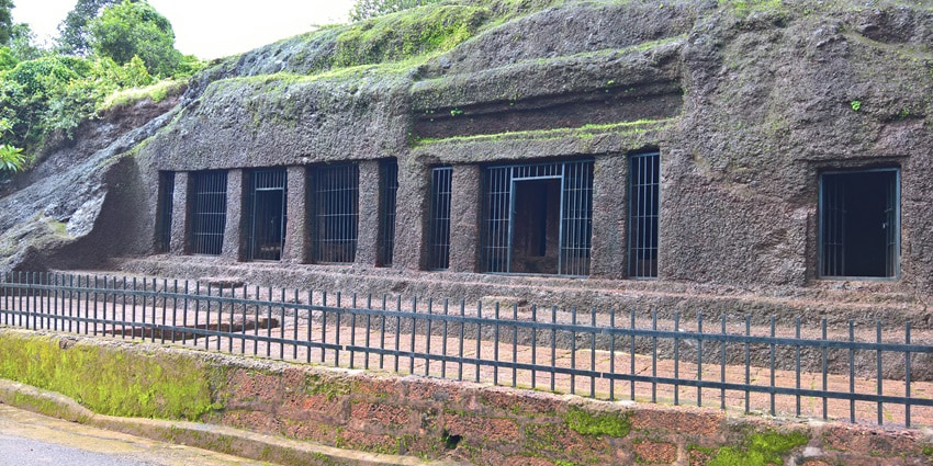 A picture of a giant rock-cut cave entrance in Goa with lush greenery all around