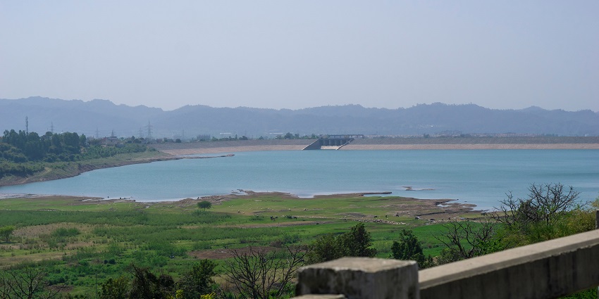 A view of a large water dam with pressurised water flowing through it during the daytime.