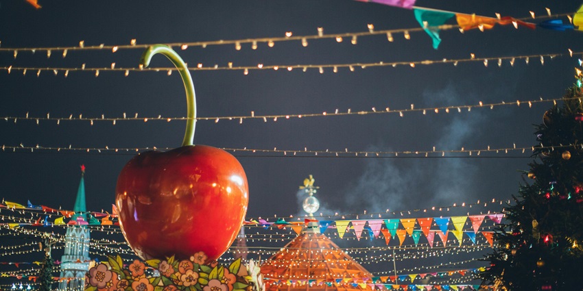 Illuminated giant red apple decoration on stall roof at colourful festival fair at night.