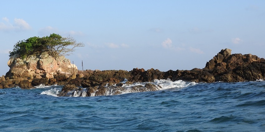 Majestic view from the island, of turquoise waters crashing on the big rocks with the blue sky in the backdrop