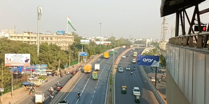 Image of Delhi roadways from a metro station with bustling traffic under blue sky