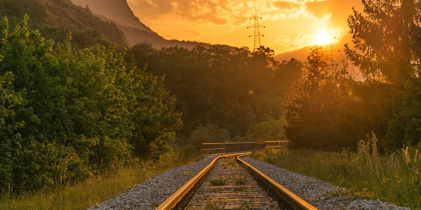 Image of railway tracks passing near lush green trees under a clear sky