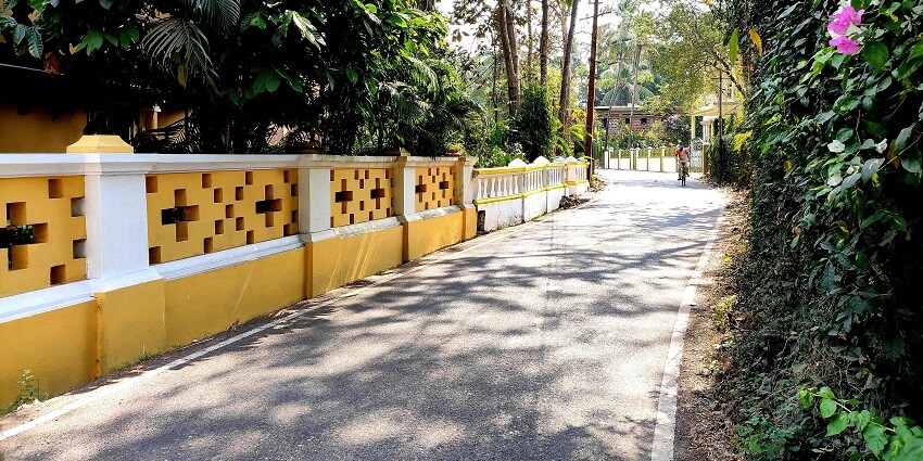 A scenic village road in Goa, India, lined with lush greenery and traditional houses