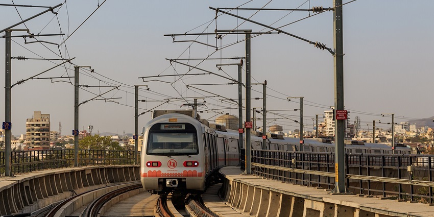A Jaipur Metro train arriving at a modern station in Jaipur, India, surrounded by cityscape.