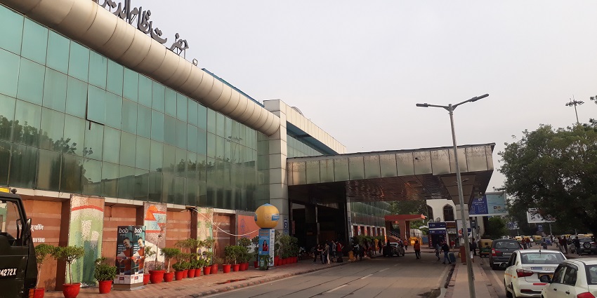 A picture of a railway station in Delhi taken from across the street with a queue of vehicles on the road