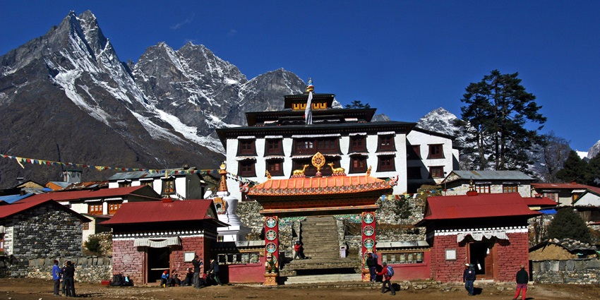 Buddhist prayer flags flutter in front of Tengboche Monastery amid snowy Himalayan peaks.