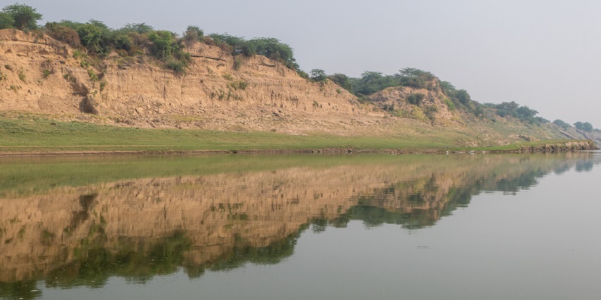A serene view of the Chambal River, with calm waters flowing between rocky cliffs and green vegetation along the banks.