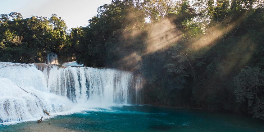 A view of a waterfall with pure blue water and sunlight shining through