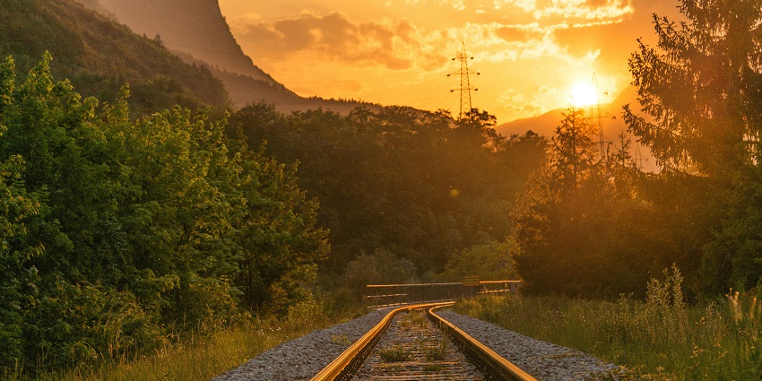 Train tracks running through a scenic area with lush green trees and clear blue skies