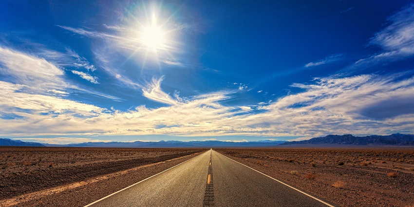 A breathtaking view of a winding road during the daytime in front of big mountains.