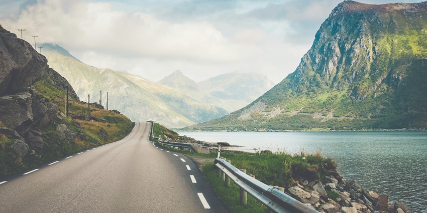 A breathtaking view of a narrow road with a water body on the side around greenery.