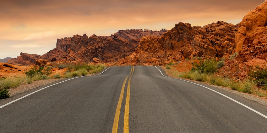 A breathtaking view of a straight road leading up to rocky hills during the daytime.
