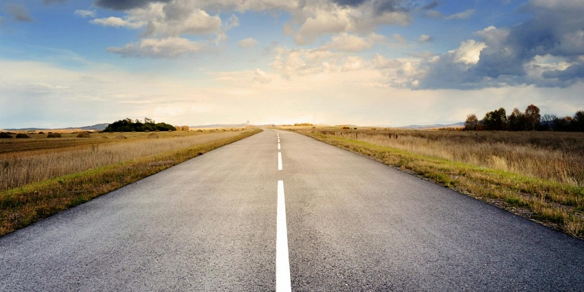 A stunning view of a road surrounded by dry grassland under dense clouds during the day.