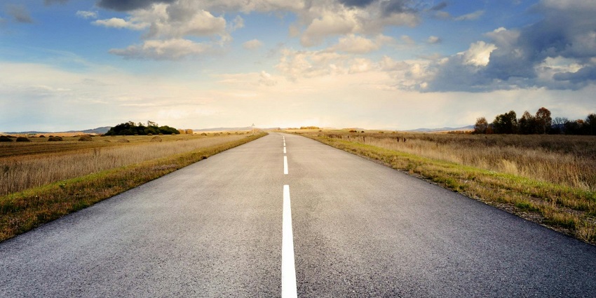 An enchanting view of a straight road leading upto lush green mountains during the day.