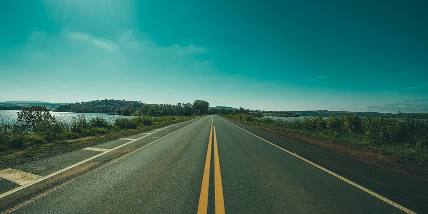 A mesmerising view of a straight road leading up to lush greenery around a body of water.