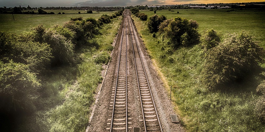 A breathtaking view of a railway track encircled by lush green meadows during the day.