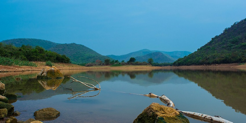 Wide angle view of a serene lake reflecting the forested hills surrounding it