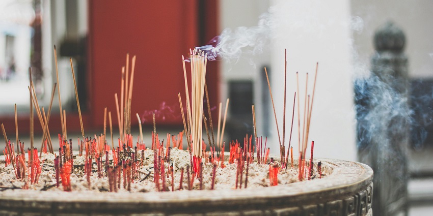 Incense sticks burning on a bed of gray ashes, releasing fragrant smoke into the air.