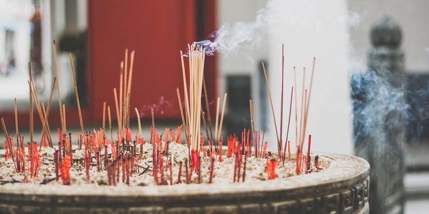 Incense sticks burning and releasing smoke, resting on a bed of grey ashes.
