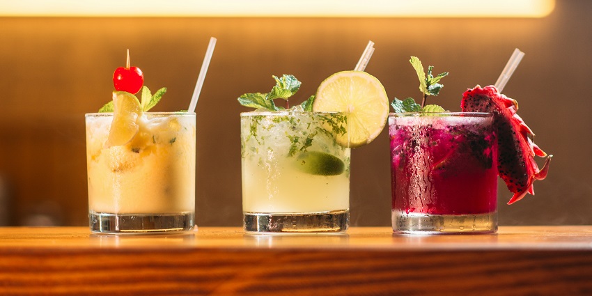 Three clear glass cups filled with colourful juice, arranged on a table with a bright background