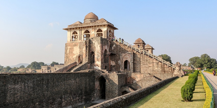 Jahaz Mahal with arched windows and domes, perched on fort walls amid manicured lawns