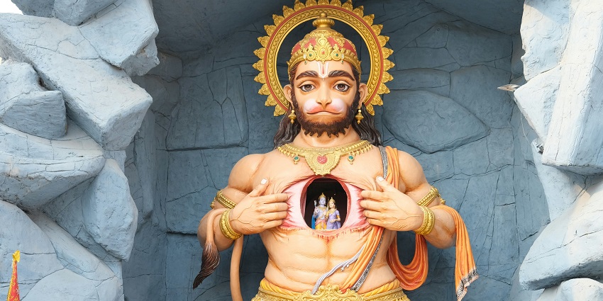 A serene statue of Hanuman ji sitting in a cave, surrounded by natural rock formations.