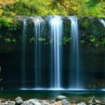 Serene lake with a cascading waterfall, captured in a long exposure during the daytime