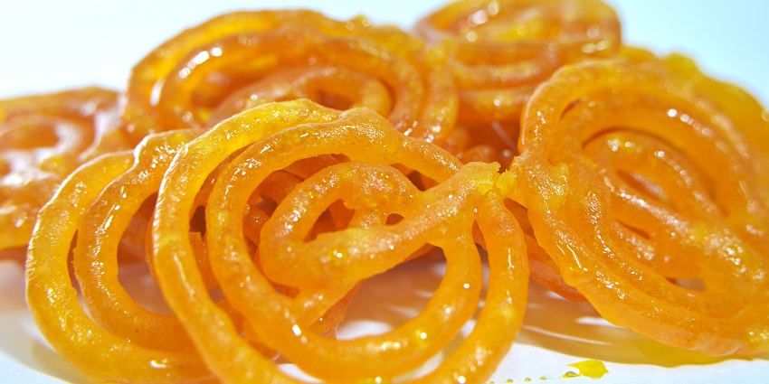 A vibrant plate of jalebi, featuring intricate, coiled shapes soaked in sweet syrup