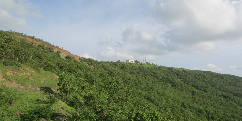 Janapav Kuti with lush green hillside covered with trees under a partly cloudy sky