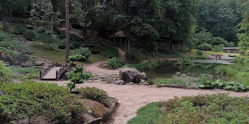 A serene garden overlooking the Arabian Sea, featuring lush greenery, paved pathways, and a secluded beach below.