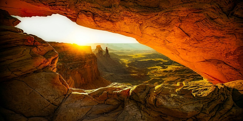 A view inside a cave with rugged rocky walls illuminated by bright sunlight streaming in.