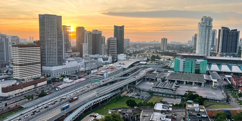 Birds eye view of a city with tall skyscrapers and cars on the road, during the sunset.