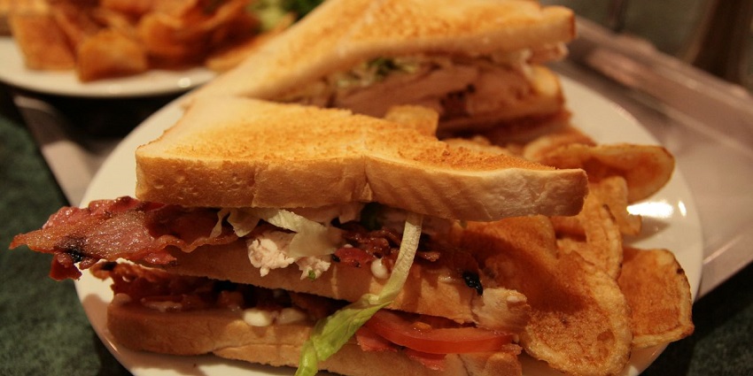 Club sandwich stacked with layers of meat, lettuce, and tomato, served with fries.