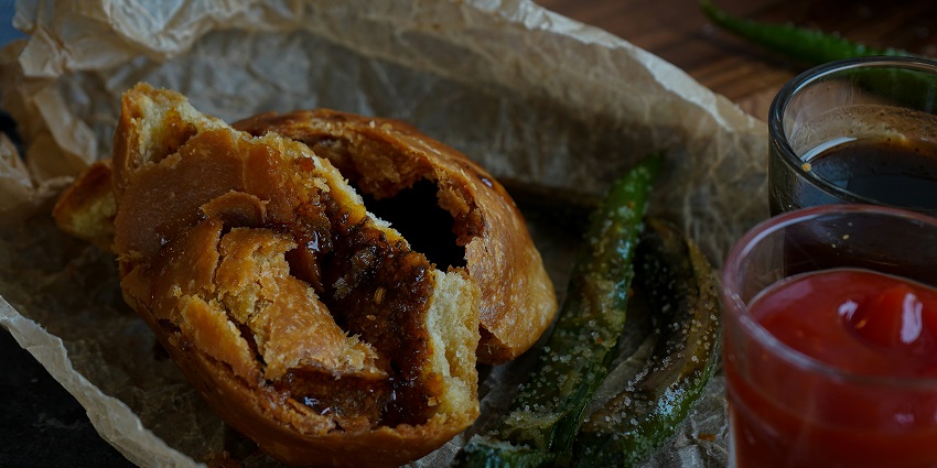A hot kachori broken in the middle with chutneys on the side for flavour.
