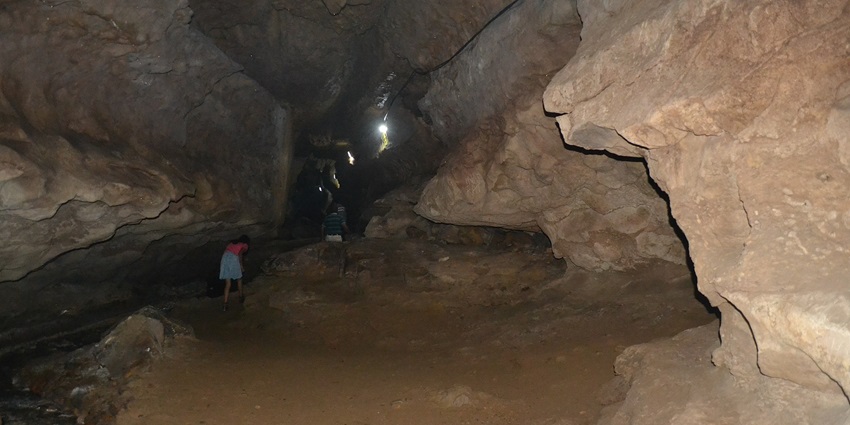 People are in a large chamber of the cave and alongside them a small river is passing by.