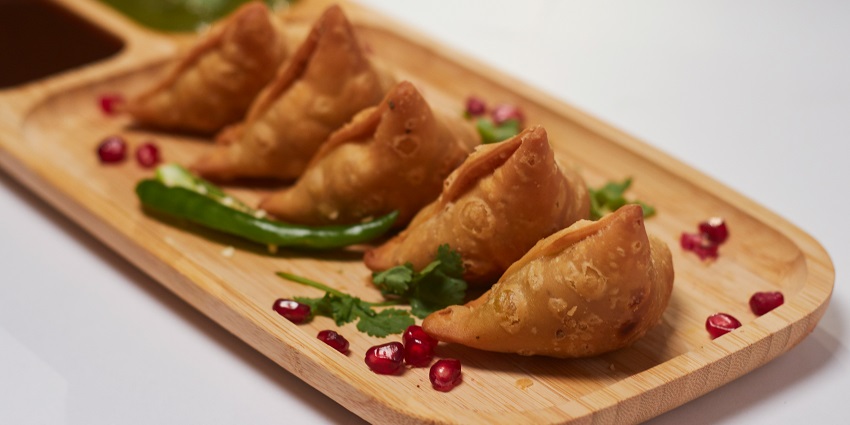 Freshly fried samosa placed on a wooden chopping board with a rustic presentation
