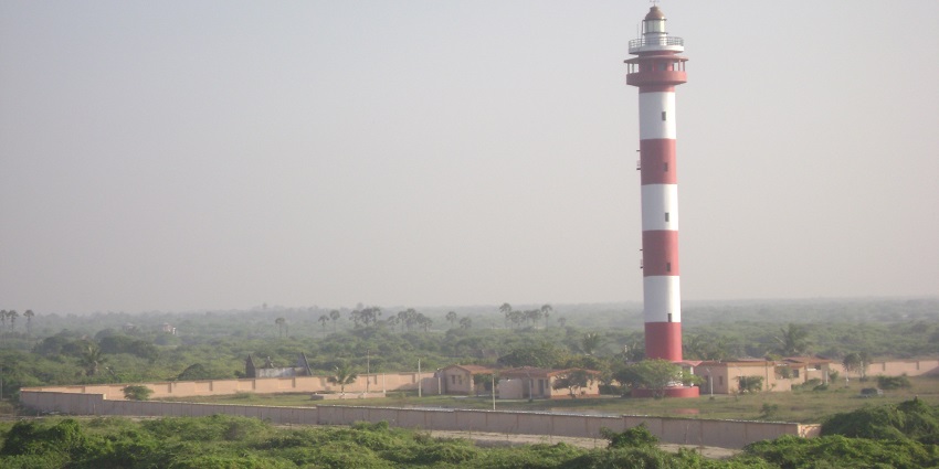 Image of a lighthouse in red and white coloured sanding tall amidst clear blue sky background