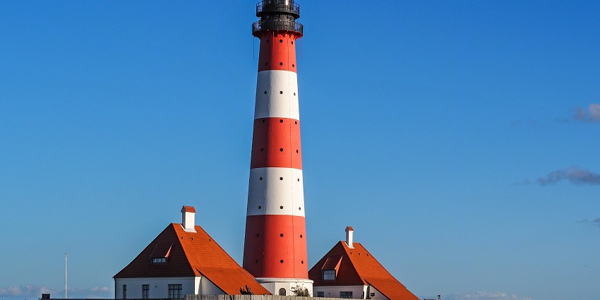 Image of a lighthouse in red and white coloured sanding tall amidst clear blue sky background