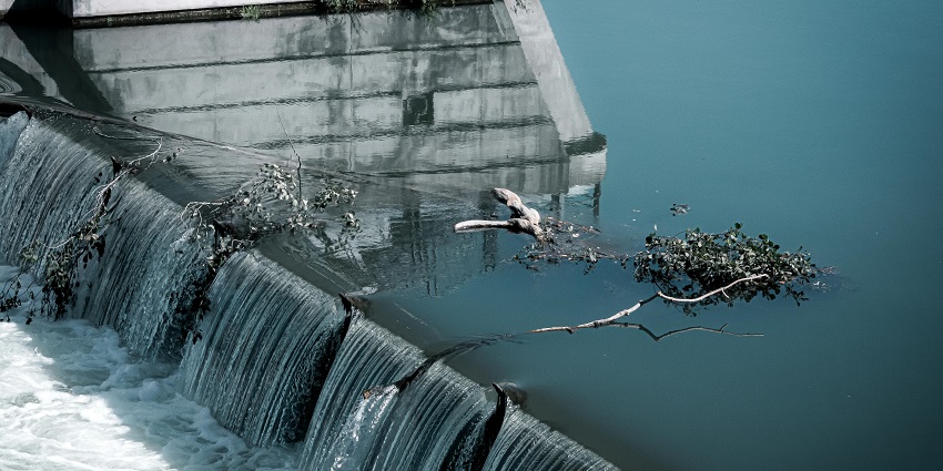 A picture of a dam with water cascading down and a small tree branch floating