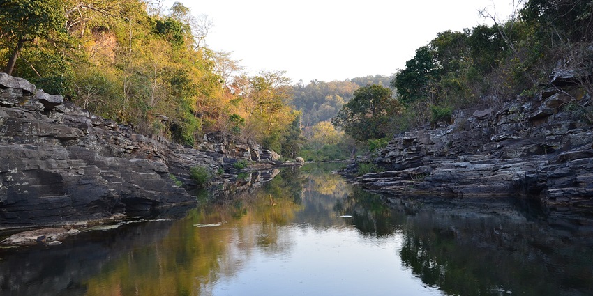 Front view of a water body reflecting the lush forest and rocks that surround it.