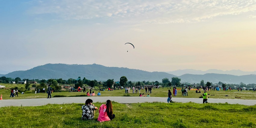 Picturesque view of people exploring and sitting on a green field surrounded by mountains